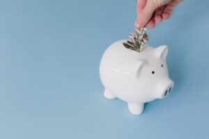 Hand putting cash into a white piggy bank, representing frugal habits that save money